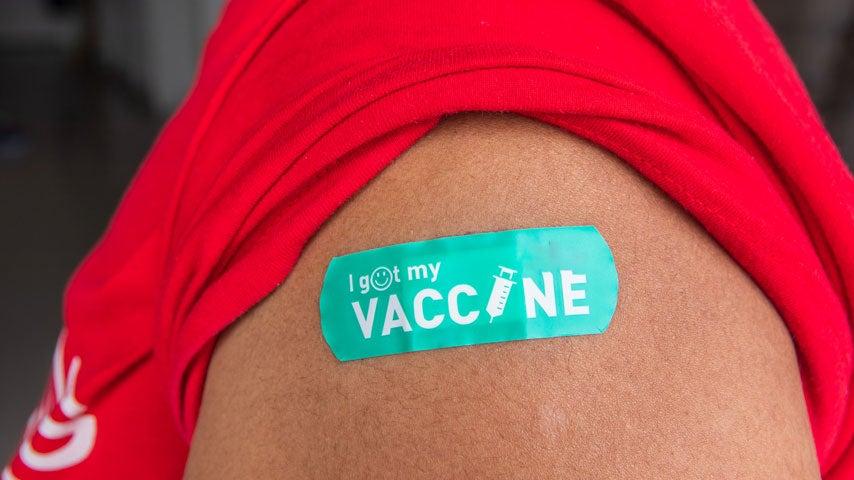 A closeup shot of a person wearing a red shirt that has a teal bandaid that says "I got my vaccine".