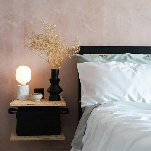 Serene and natural bedscape with a bedside table, lamp, and fluffy white sheets on the bed