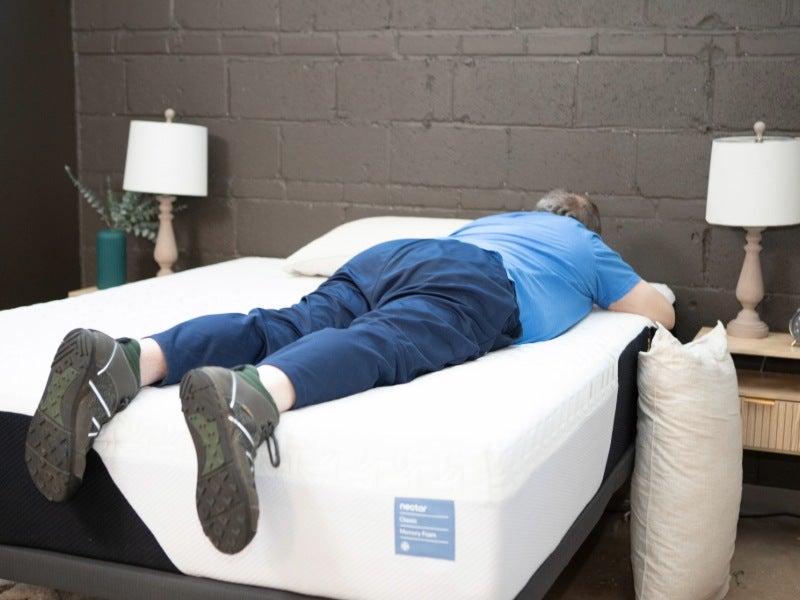 A man lays on his stomach on a bed with his feet dangling off the edge.