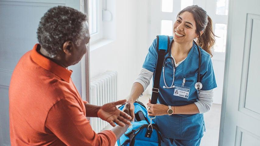 nurse with bag and stethoscope shaking hands with older Black man in his doorway