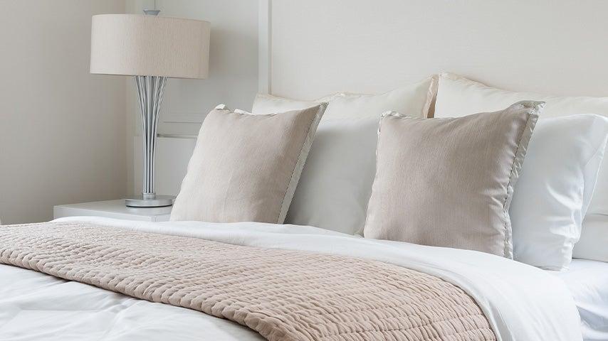 Bed and nightstand with beige and white bedding and lampshade