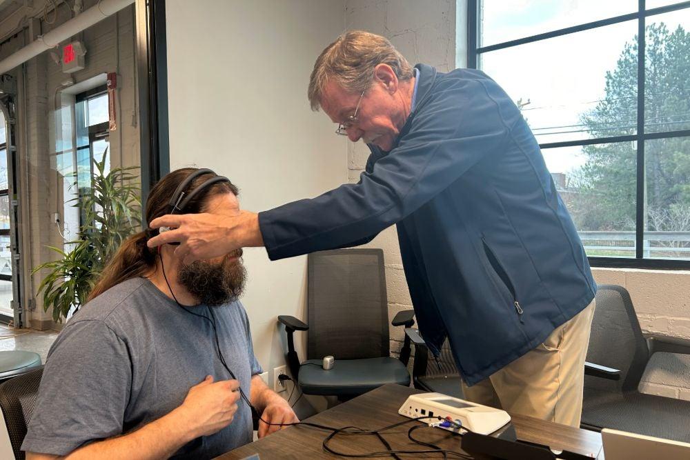 A hearing instrument specialist placing headphones on another man’s ears