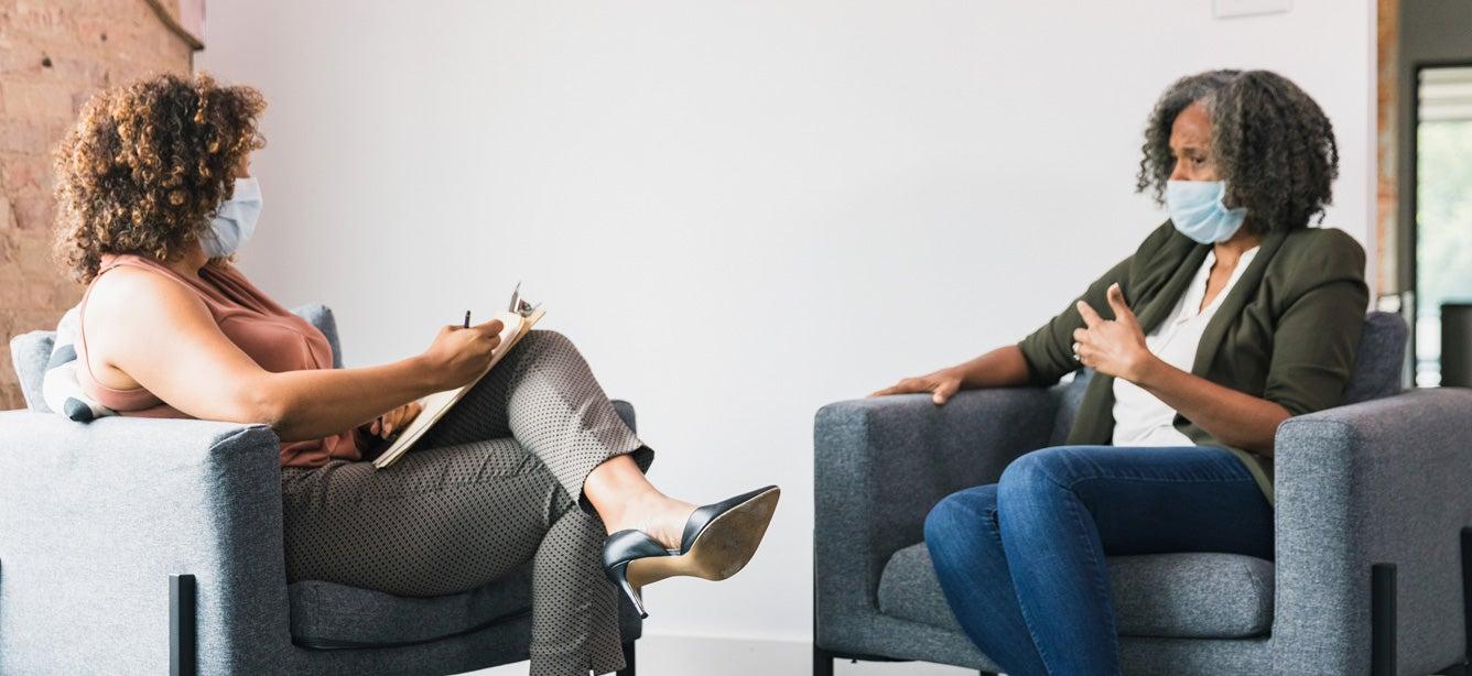 A senior mental health patient wearing a mask is talking to her behavioral therapist.
