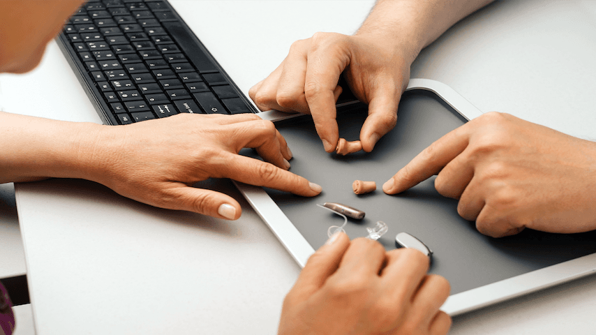 close up of hands holding and pointing to small hearing aids