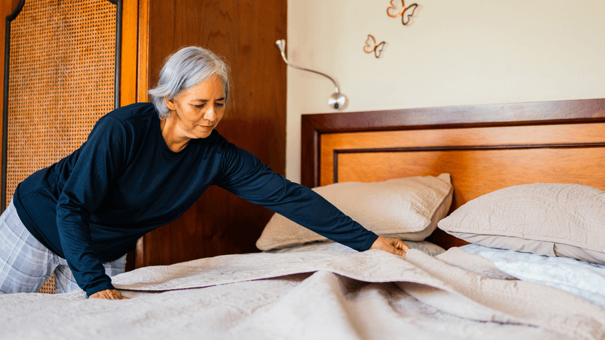 An older woman makes her bed