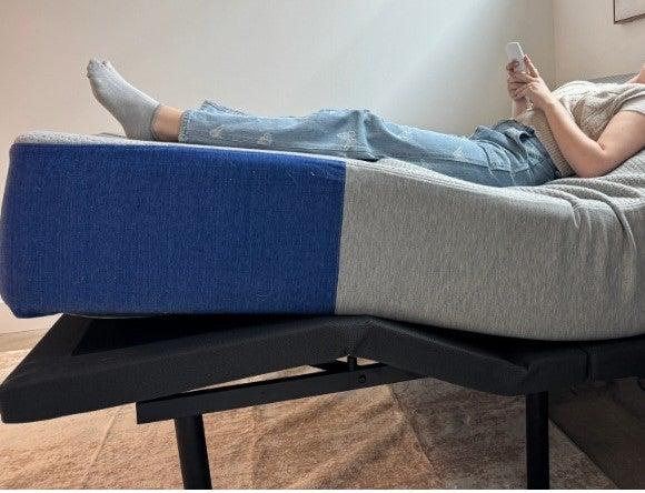 A woman lying on the Nectar Adjustable Base while holding its remote