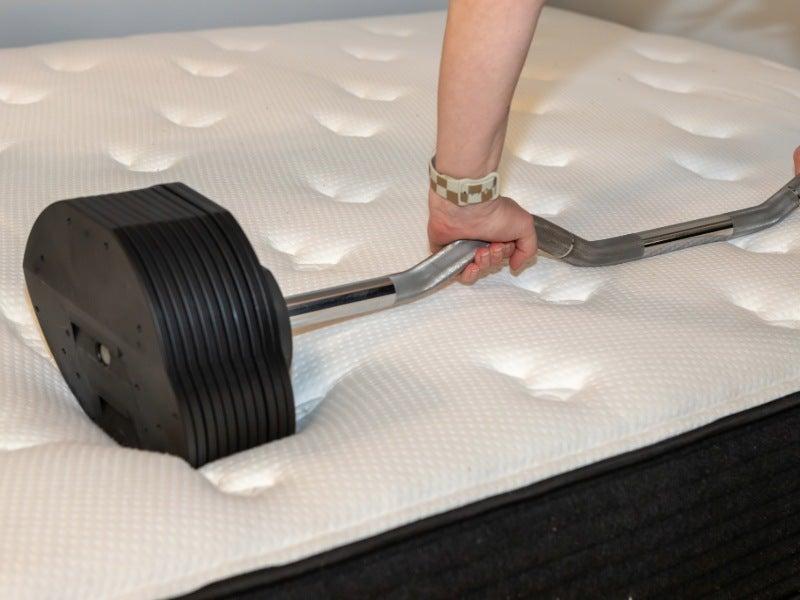 A person rolls a large barbell across the surface of a mattress