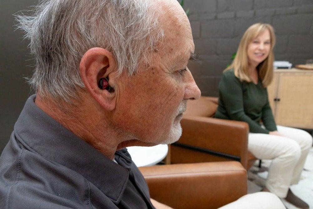 close up of man with hearing aid in left ear, smiling woman in background