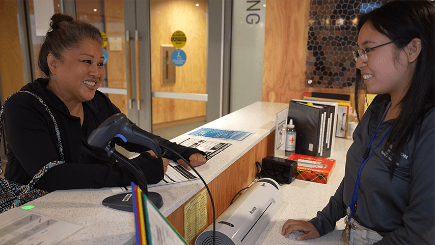 smiling older woman checking in with front desk staff at senior center