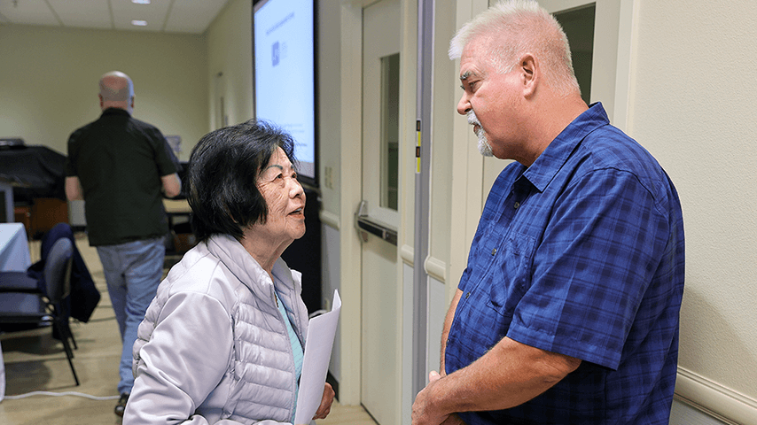 older Asian woman talking to older white man