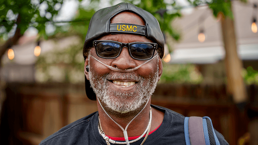 smiling older man wearing USMC baseball cap and oxygen tubes in nose