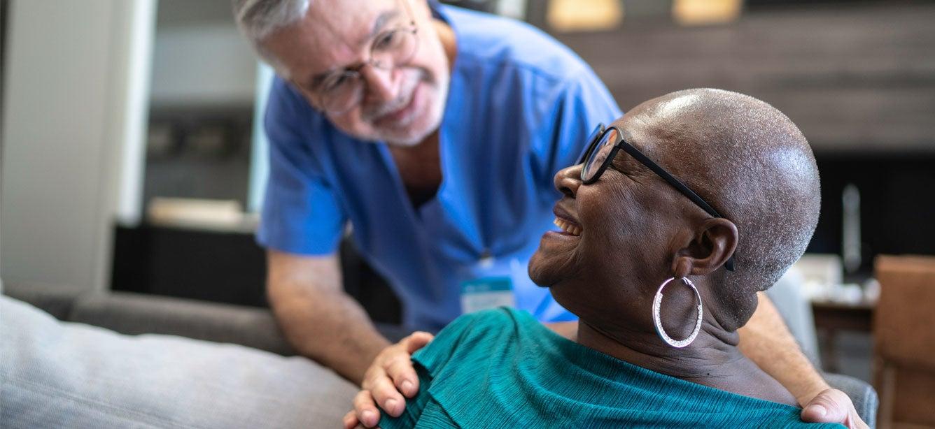 A senior Black woman is chatting with her home caregiver, smiling as they have a discussion.