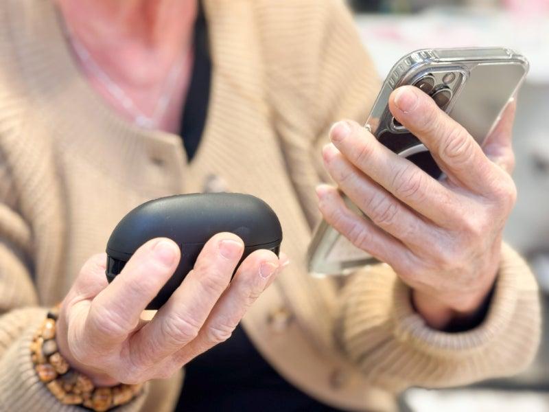 A woman holding the Soundbright hearing aids in one hand and a smartphone in the other