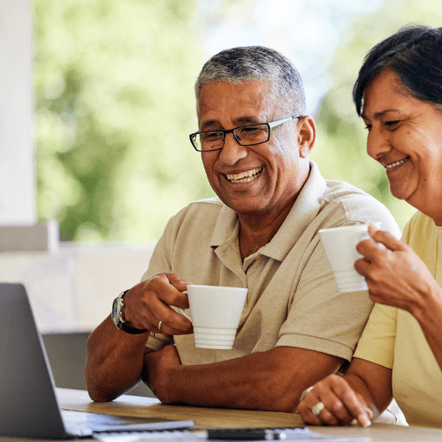 Man and woman smile while drinking coffee and looking at a laptop