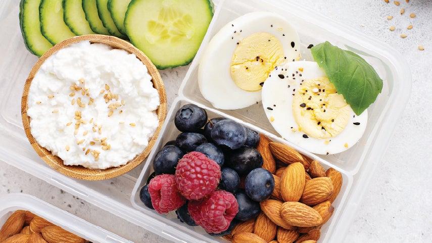 Beautiful spread of a balanced meal with healthy protein options, including cottage cheese and cucumbers, a hard boiled egg, and berries and almonds.