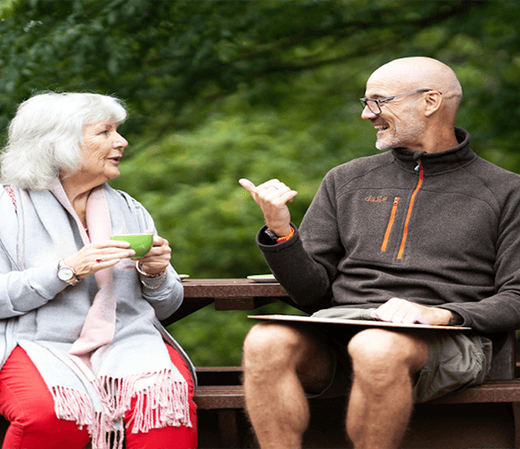 older bald man and older woman with gray hair talking on park bench