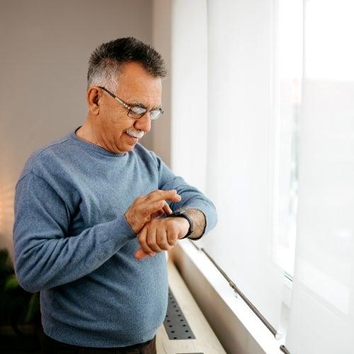 A man standing in front of a window pressing the buttons on a smartwatch