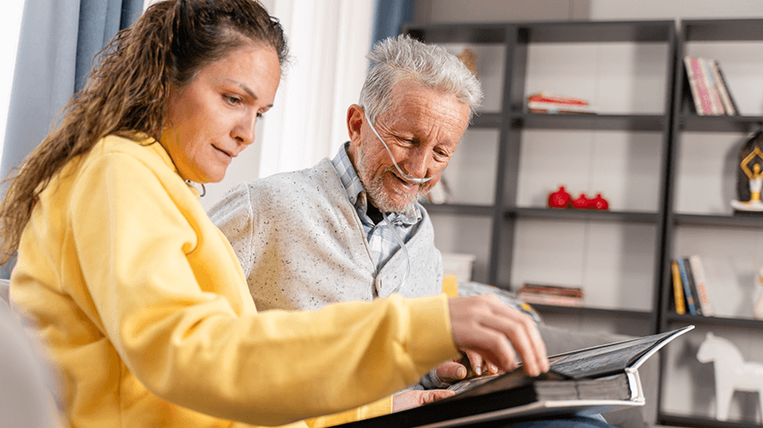 older man with oxygen cannula looking at photo album with woman