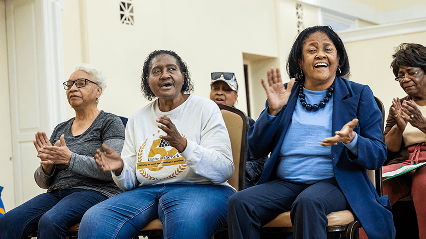 five seated older women clapping and singing