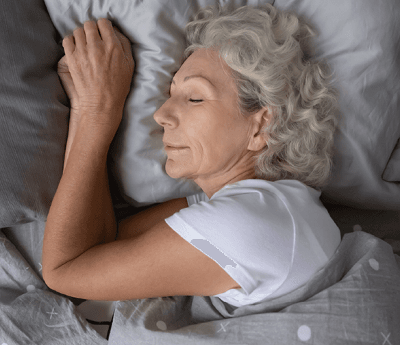 woman with wavy gray hair sleeping on gray sheets and pillowcase