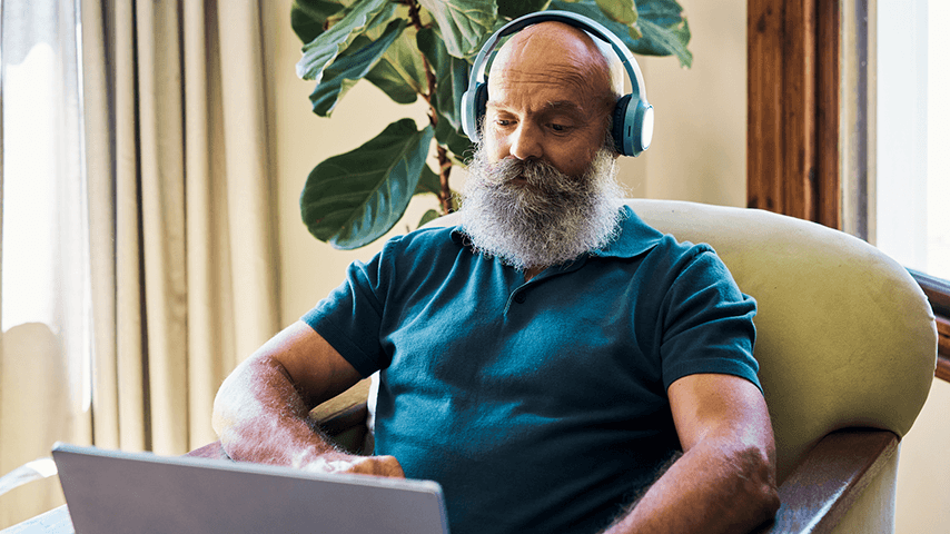 man with bushy gray beard and mustache wearing headphones and looking at laptop