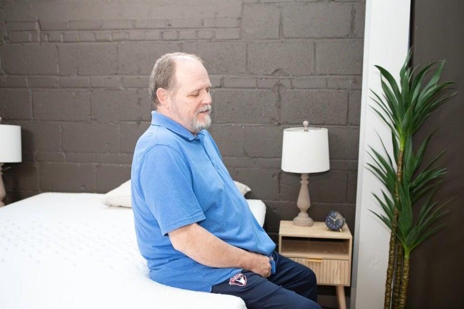 A man sits on the edge of the Nectar Premier Memory Foam mattress.