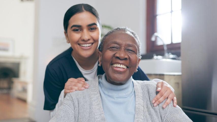 younger woman care worker smiling with hands on shoulders of smiling older black woman