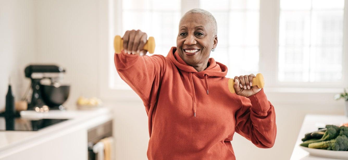 A senior black woman is doing strength exercise with dumbbells in her home.