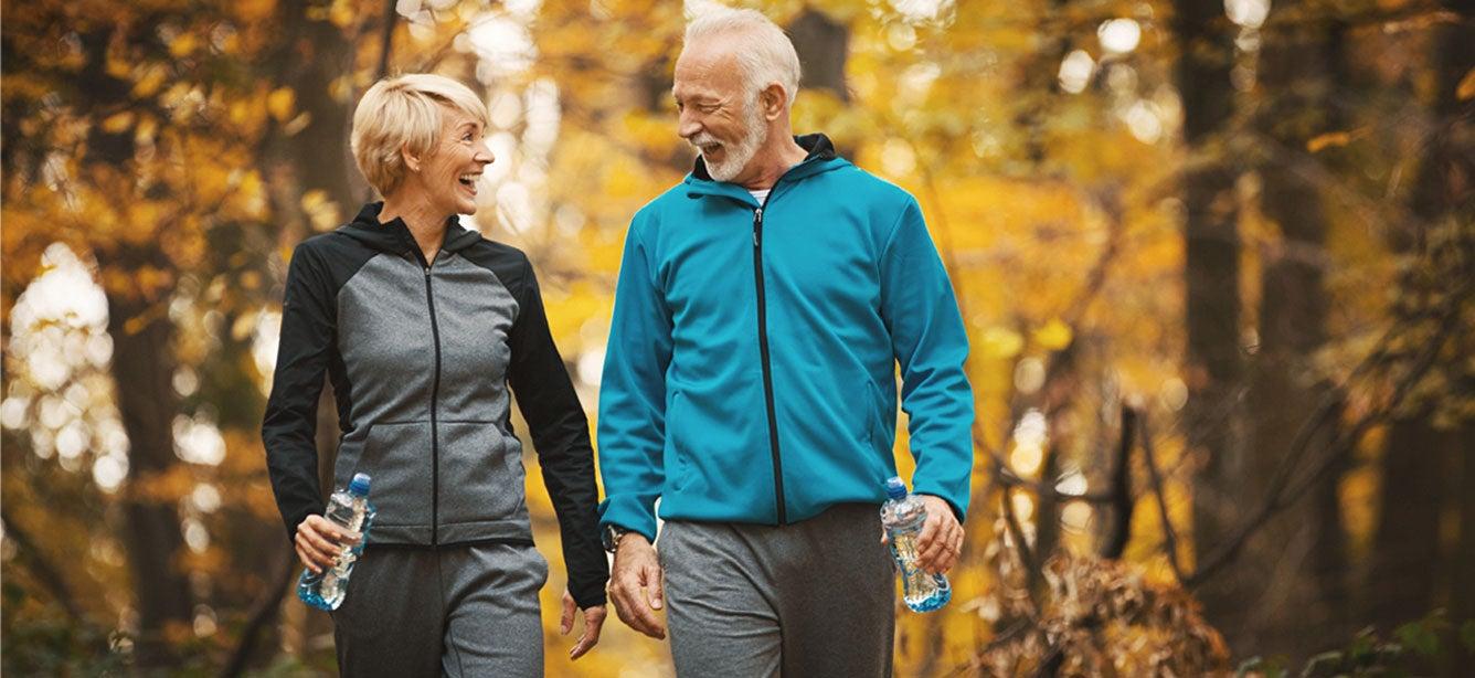 A smiling older couple walks together in a forest.