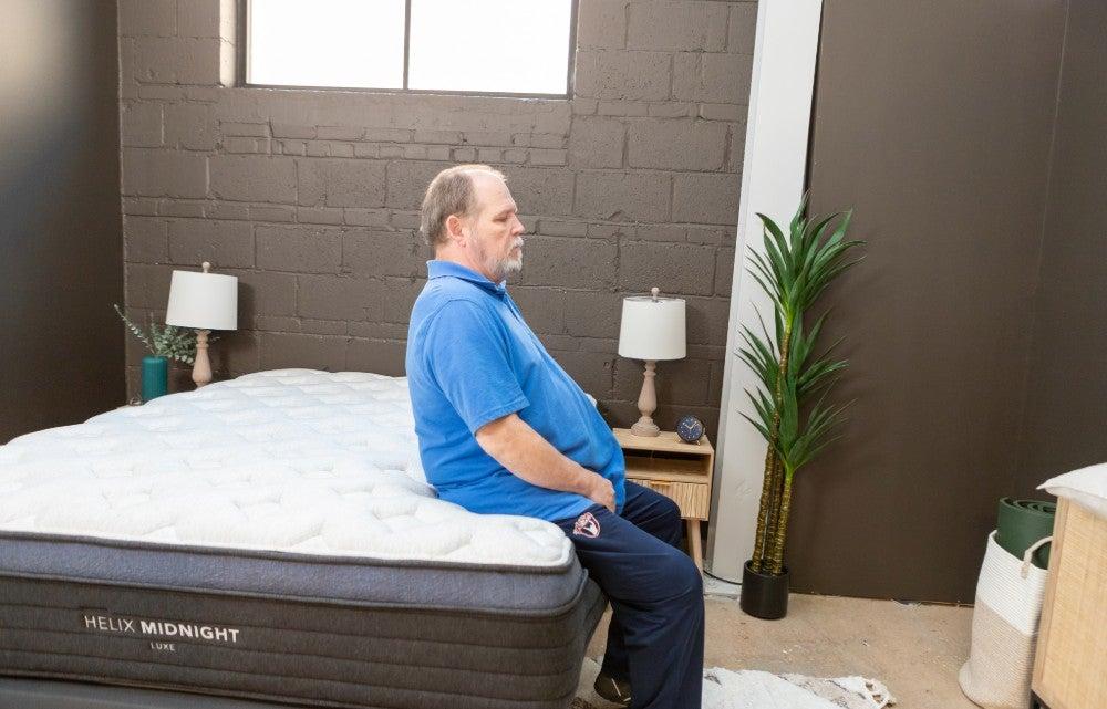 Man sits on edge of Helix Midnight Luxe mattress