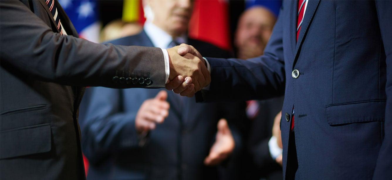An elected official is shaking hands with an event organizer as an audience applauds.