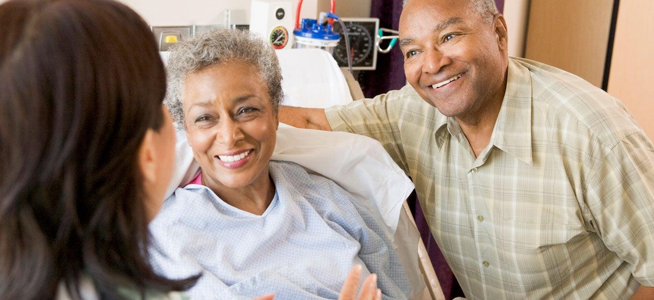 A black senior couple is at the hospital, speaking to the doctor before the senior woman's surgery.