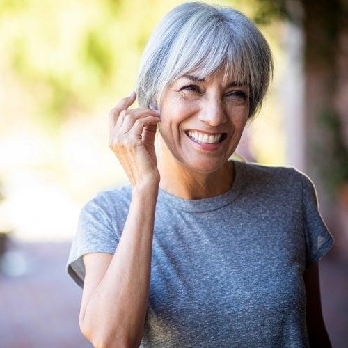 A smiling woman with short silver hair touches her ear