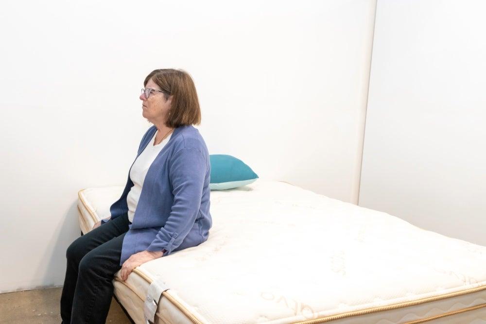 A woman sitting on the edge of the Saatva Classic mattress