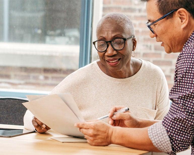 An older Black female professional is discussing Medicare benefits with an Asian male colleague.