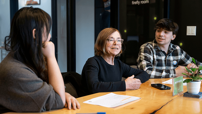 older woman talking to younger man and woman at conference table