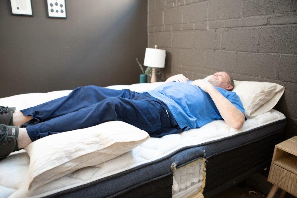 An older man lying on his back with a pillow under his knees