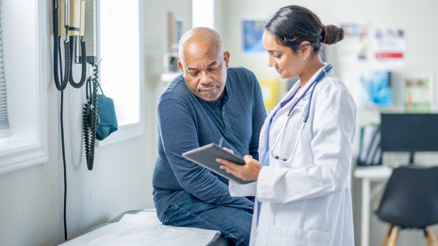 A younger doctor is showing a Black older man information about the shingles vaccine on her tablet.