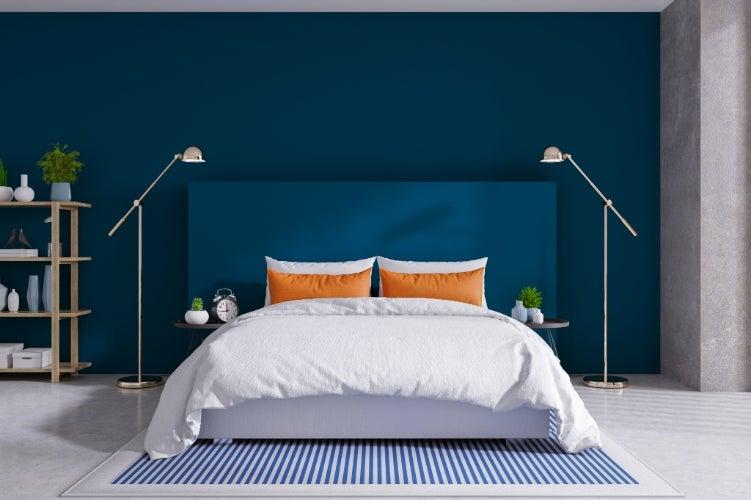 A bed made up with a white comforter against a blue wall