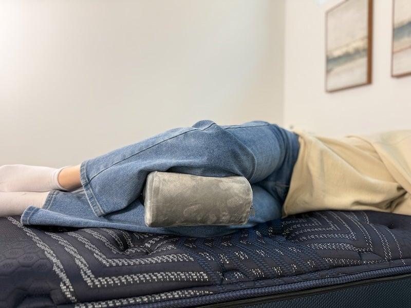 A person rests on their side with the grey Sleep Number Knee Pillow between their legs