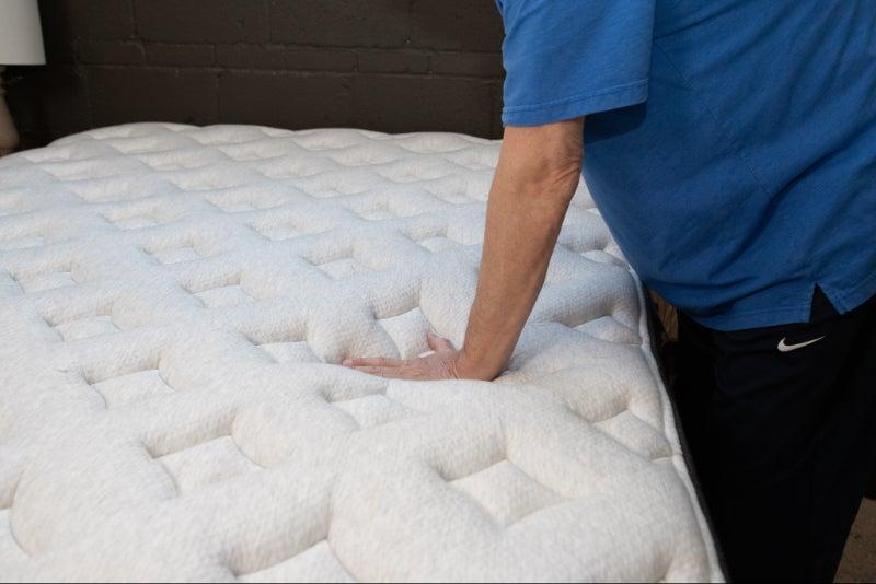 A man presses down on the cover of the Helix Midnight Luxe mattress