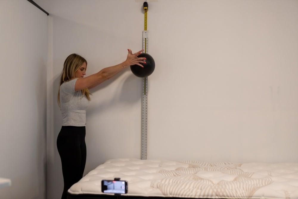 A woman holds a weight above the Nolah mattress in a test to measure its bounce