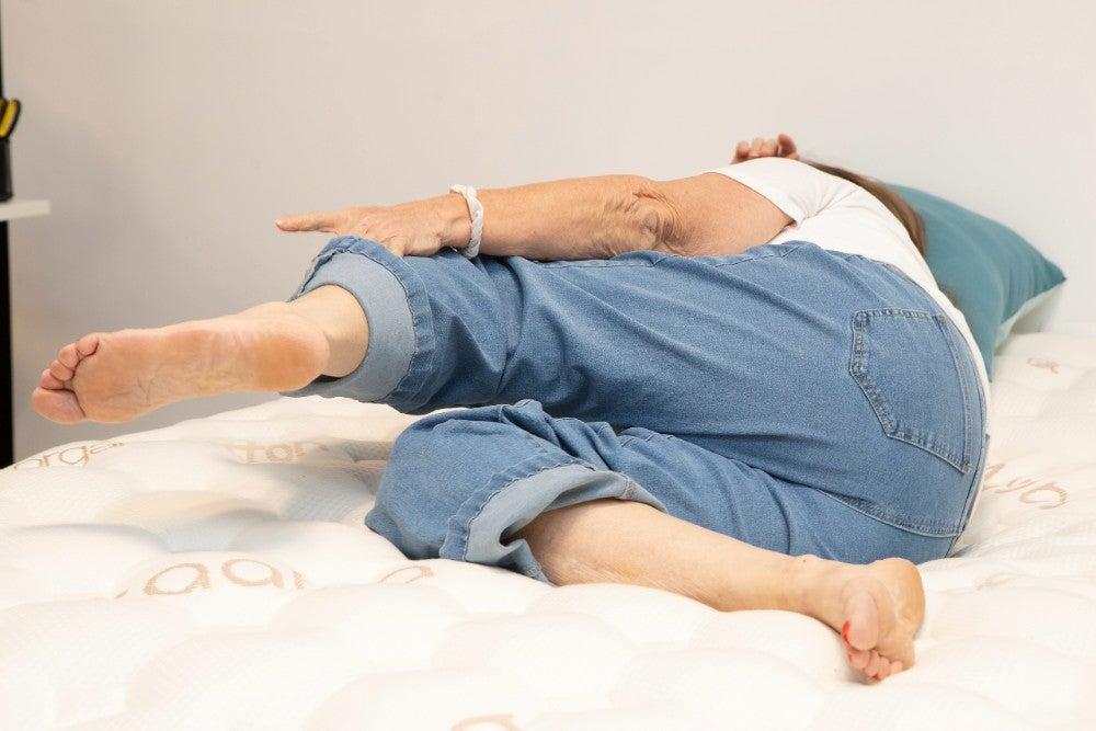 An older adult tester changes positions on top of the Saatva Rx mattress