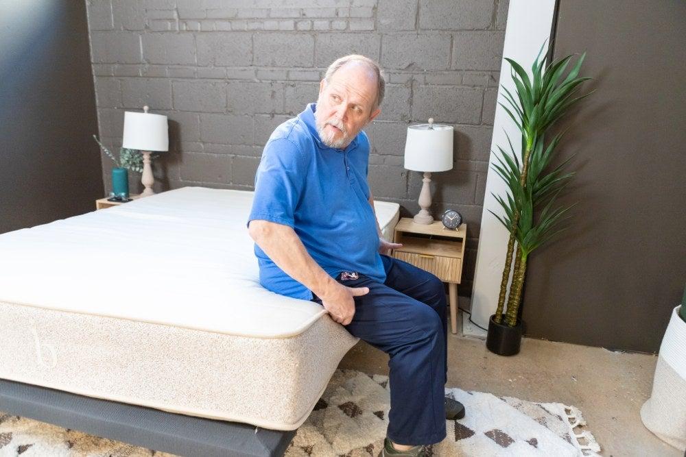 Man sits on the edge of the Birch Natural mattress with his feet on the floor