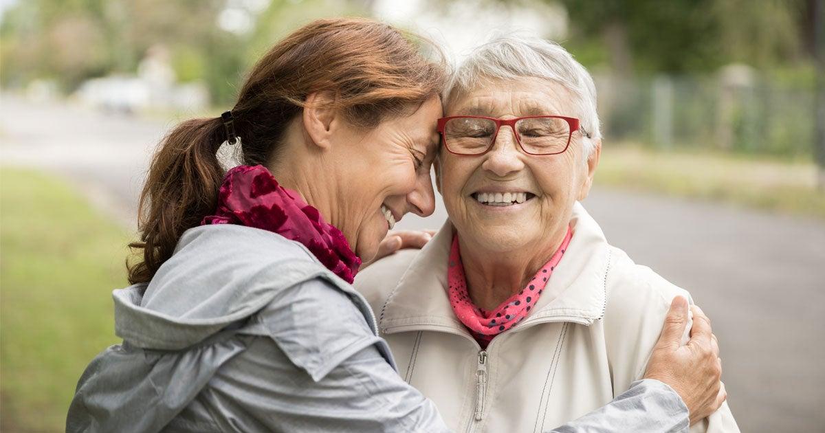 A middle-aged woman embraces her mother while they're standing outside in the park.