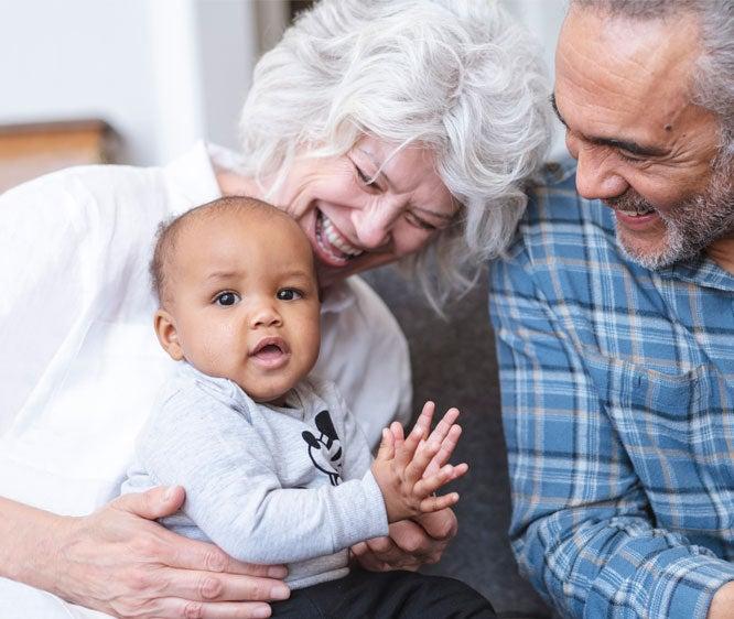 An interracial senior couple is playing with their grandson in their living room.