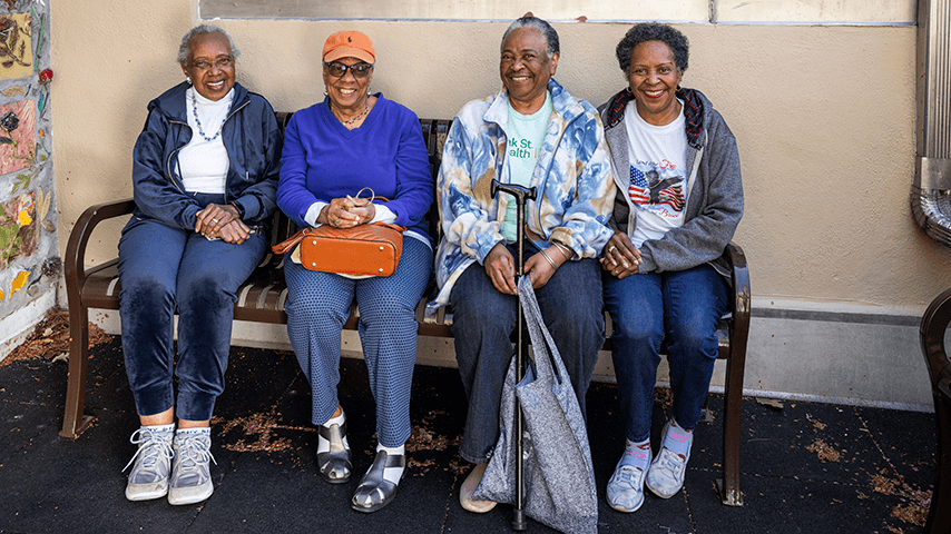 four smiling older Black woman sitting on outdoor bench