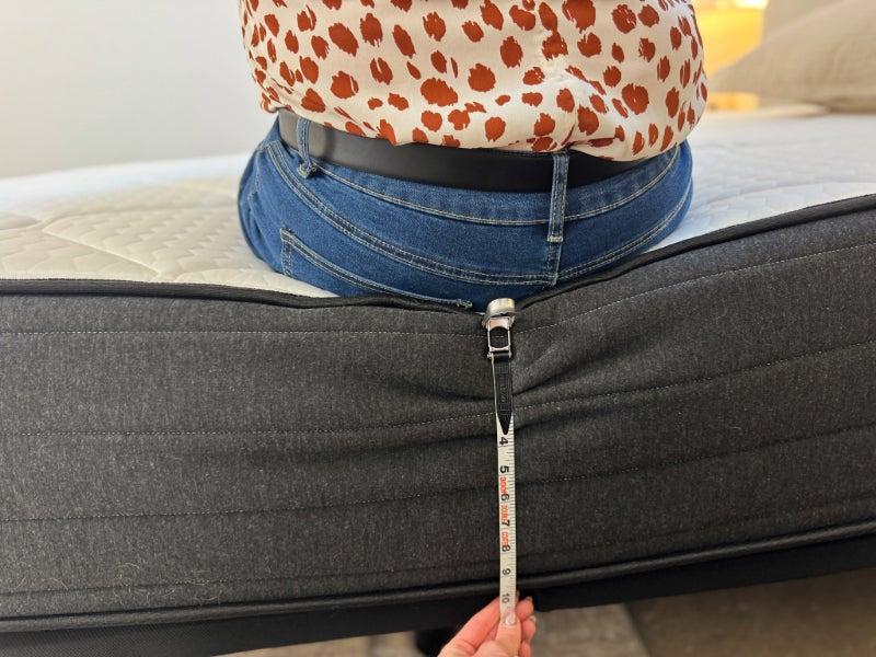 A person measuring the side of the Plank Firm Luxe mattress as another person sits on the edge