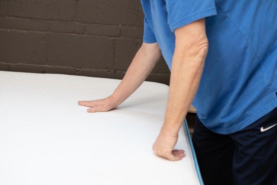 A man touches the surface of the Bear Original mattress, which has a cooling cover.