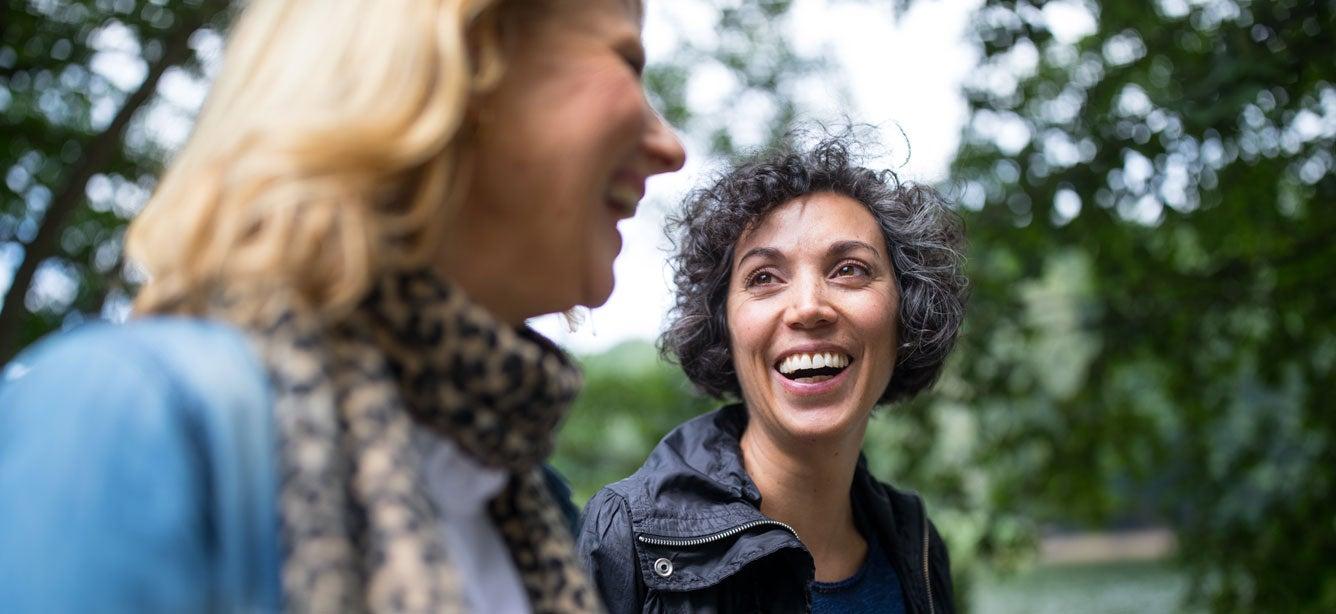 Two women smiling and chatting outdoors, surrounded by lush greenery.